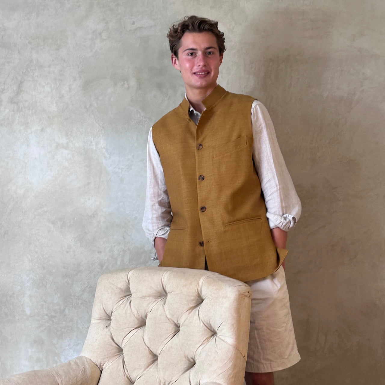The perfect alternative to a jacket on hotter days. Tan coloured slim fit gilet in a summer weight silk weave. Handmade in London this fitted waistcoat has five pockets and a Nehru collar. Made in Great Britain. Modelled over cream co-ordinates.