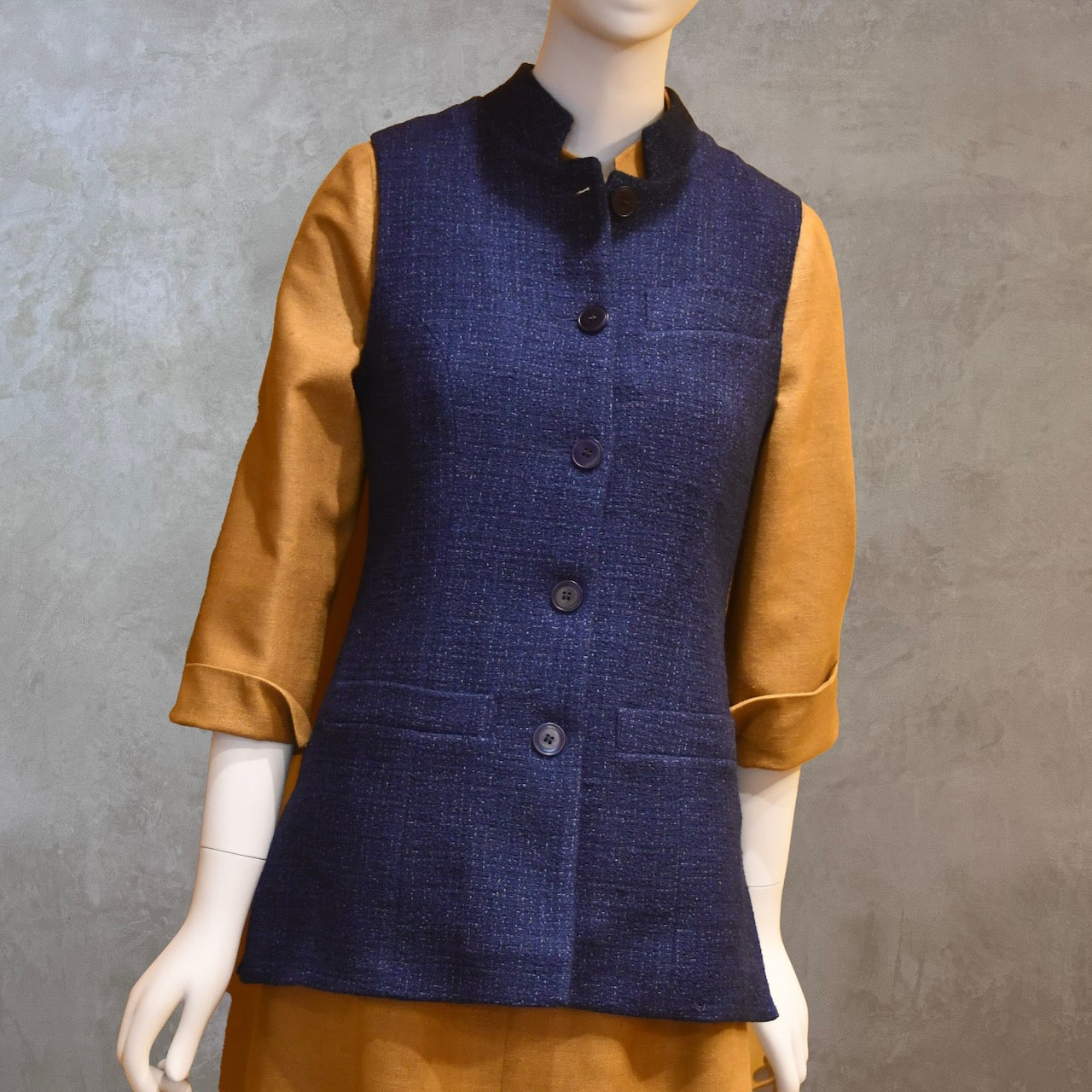 Full Front Shot of Longer Length Ladies Waistcoat in Linton Tweeds Boucle. A pure cotton weave, this is superbly trans-seasonal option. Handmade in London. Shown worn over mustard coloured silk Matka Dress from Ednerat.