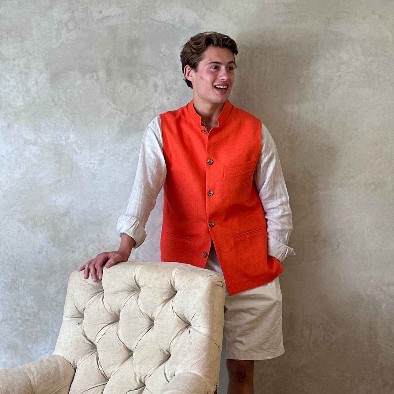 Modelled shot of Slim fit nehru style gilet in summer weight silk weave fabric. Handmade in London, this orange silk matka fitted waistcoat has a Nehru collar, Courtney & Co buttons and is fully lined in striped cotton ticking.