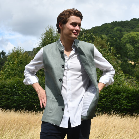 Slim cut summer weight nehru style gilet in pale green silk weave. Handmade in London this fitted waistcoat has a Nehru collar and is fully lined in cotton ticking. Real horn buttons. Shot outside in summer.