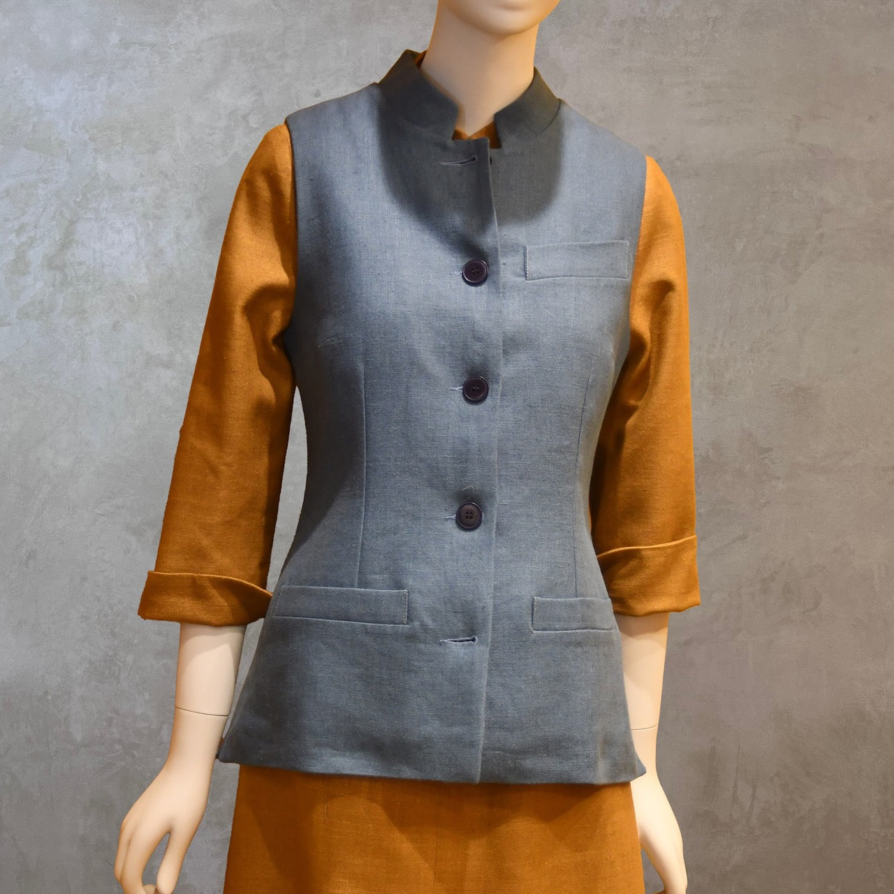 Ladies Gilet in Light Blue Irish Linen. Handmade in London this waistcoat has a Nehru collar, cotton ticking lining, bust darts as well as front and rear waist-shaping darts. Shown over mustard coloured EdNerat dress.