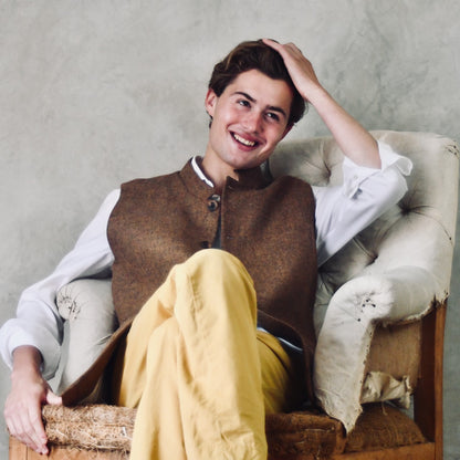Fitted Cut Nehru Style Gilet in Brown finely woven Yorkshire tweed. Handmade in London, this gilet has five buttons to the front, a Nehru collar. three outside and two inside pockets. Smart and wearable in both Town and Country. Seated Relaxed View.
