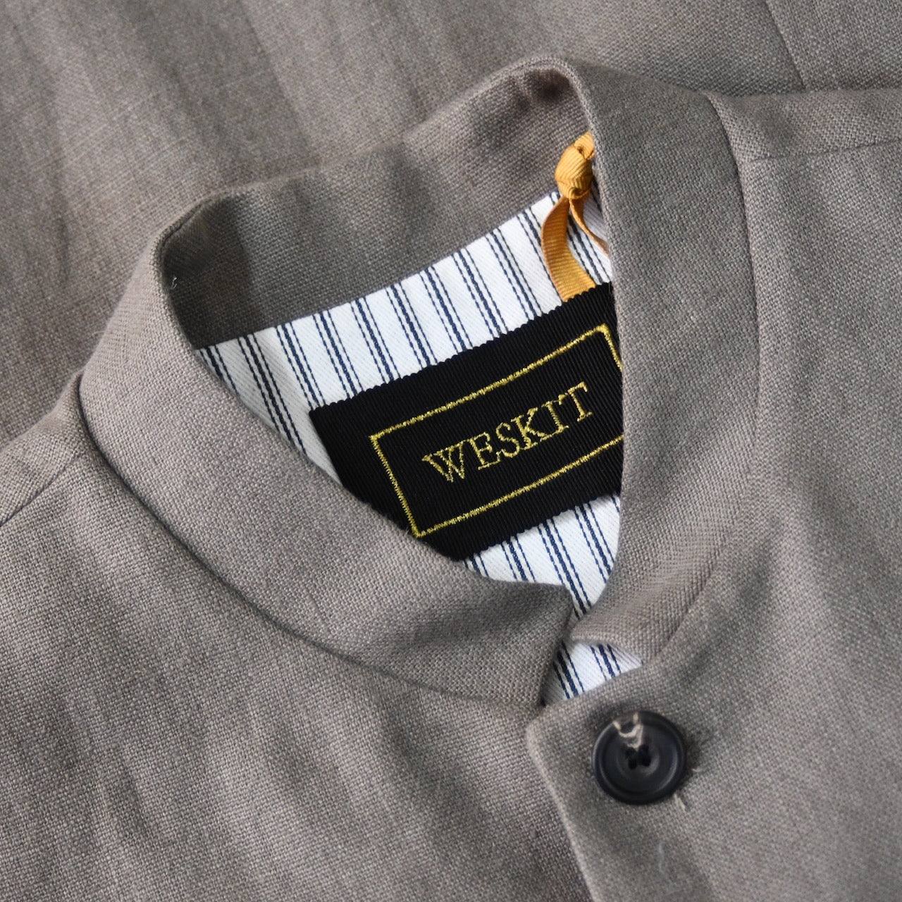 Collar detail showing Nehru collar and black embroidered label on Nehru-style fitted gilet in relaxed brown Irish linen. Handmade in London this slim-cut waistcoat has a Nehru collar, is fully lined in pure cotton ticking and has five pockets. Standing buttoned shot.