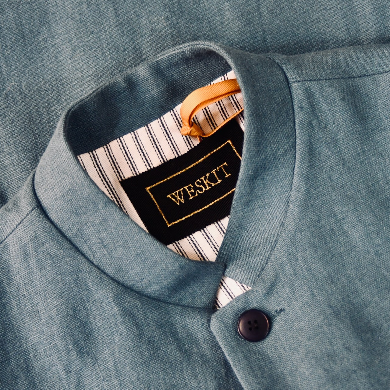 Close up on collar of Light blue Slim cut linen gilet from Weskit. Handmade in London, this slubby linen waistcoat is made in pure Irish linen and lined in striped cotton ticking. Mandarin collar and Courtney and Co buttons. Entirely made in Great Britain. Buttoned Side View.