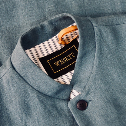 Close up on collar of Light blue Slim cut linen gilet from Weskit. Handmade in London, this slubby linen waistcoat is made in pure Irish linen and lined in striped cotton ticking. Mandarin collar and Courtney and Co buttons. Entirely made in Great Britain. Buttoned Side View.