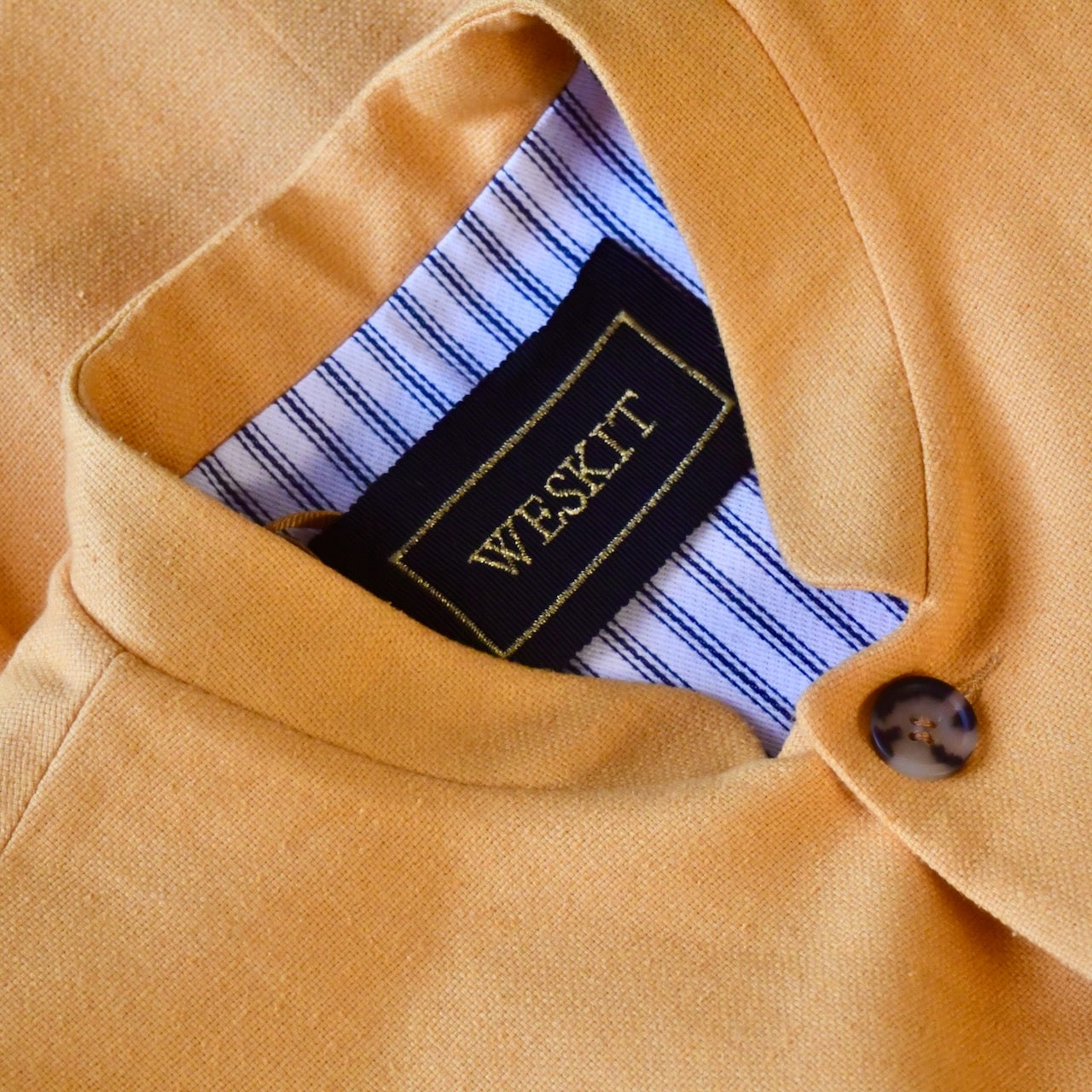 Close up collar view of summer weight slim-fit gilet in bright yellow silk weave. Handmade in London this tailored cut waistcoat has a Mandarin Collar, Striped Cotton Ticking Lining and five buttons to the front. Made in Great Britain. Showing Mandarin Collar, black and gold silk label and cotton ticking lining.