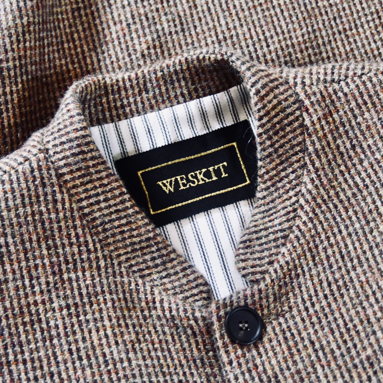 Collar Detail showing a Mandarin collar, striped cotton ticking lining and a black silk embroidered Weskit label. A wonderfully warm Nehru-style gilet in a thick tweed from Hawick. Designed in Wales, oven in England, handmade in London with buttons from Gloucestershire, this is a truly British Waistcoat. Detail Shot. Side vents for ease and five pockets for storage!