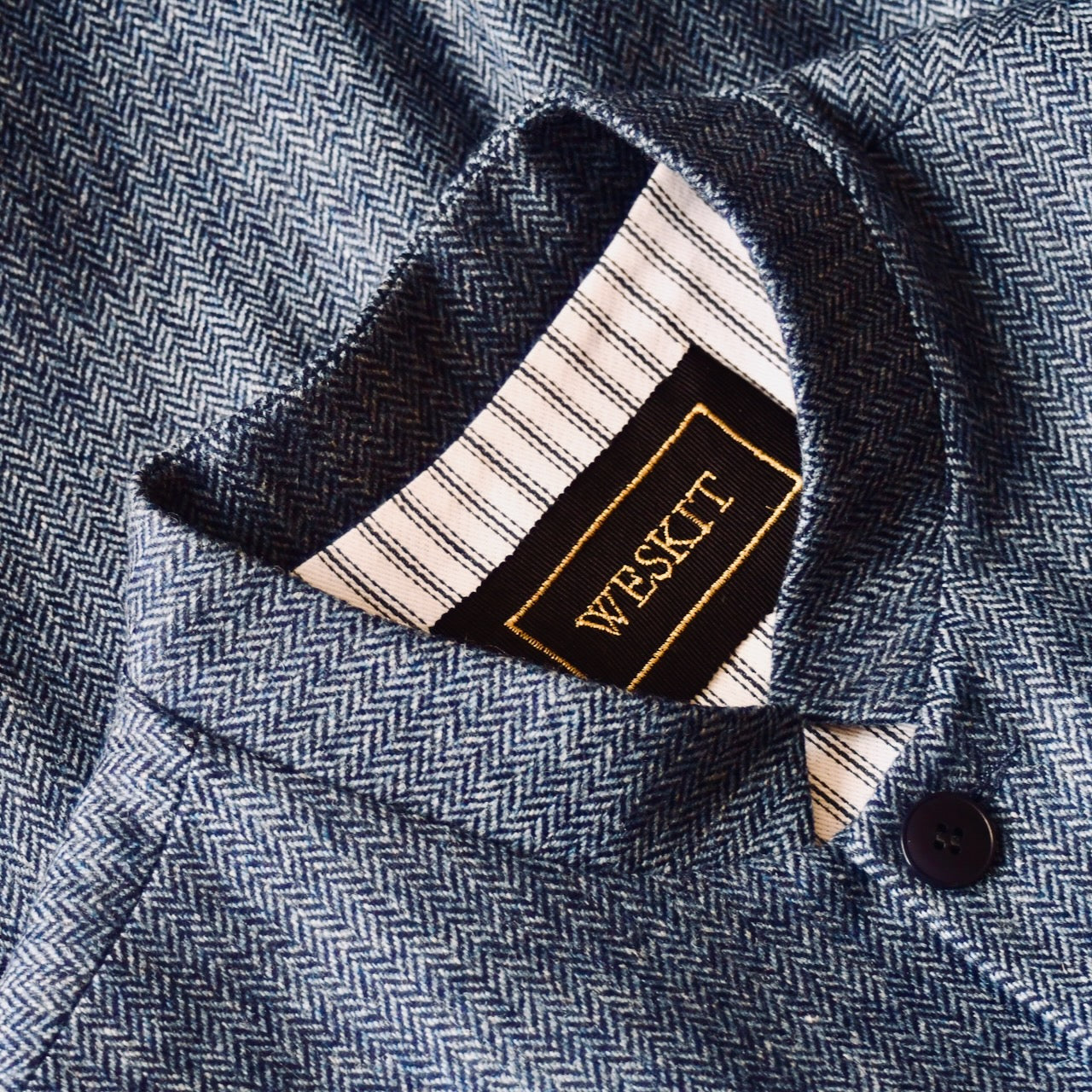 Collar Detail and Fabric Close Up on Fitted Cut Nehru-Style Gilet in Denim Blue Herringbone Tweed. A Tailored Cut waistcoat in magical mid-to-warmer weight lambswool tweed with a herringbone patterning.
Giving the overall effect of a delightful denim from a distance, this textiles brightens up on closer inspection as the depths and vivid colours of its patterning are revealed.
Smart, elegant and urbane – but as easy to match with jeans as it is to wear more formally.