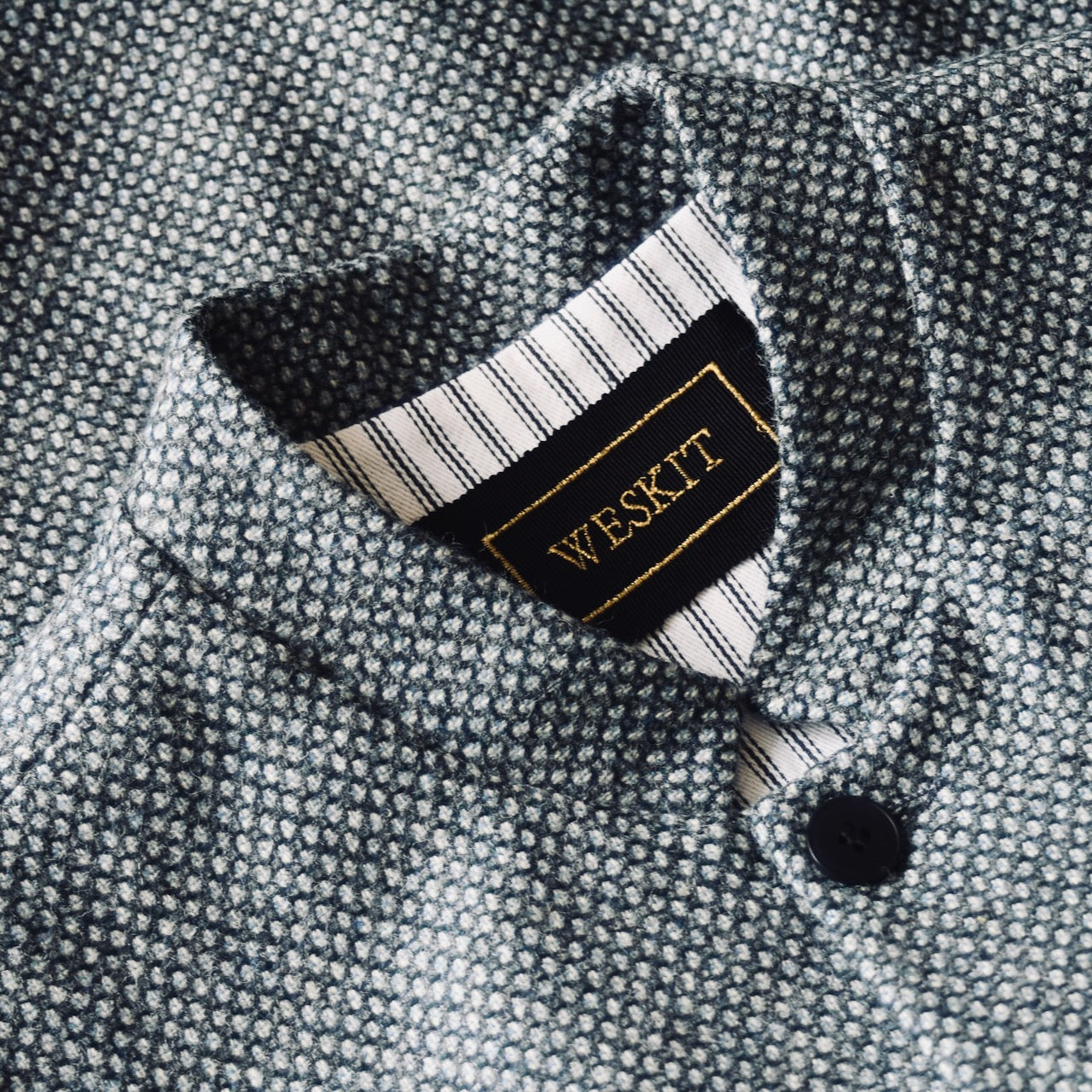 Collar Detail on a magical limited edition mid-weight Tailored Cut waistcoat in light grey and blue tiger eye tweed. This tightly woven Yorkshire tweed has an usual patterning giving the overall effect of a mid blue from a distance, it lightens and brightens up on closer inspection as the depths and vivid colours of its patterning are revealed.
Nehru Collar, Striped Ticking lining and a Flat Horn button.
Entirely made in Great Britain.