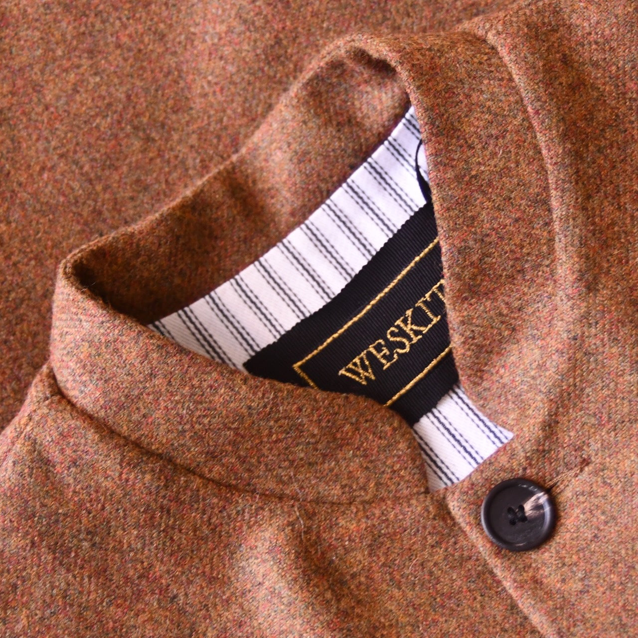 Collar detail showing striped cotton ticking lining and embroidered label on Fitted Nehru style gilet in a lovely orange brown Yorkshire tweed. Three outside and two inside pockets make this a splendid alternative to a jacket. It can be dressed up or down and the finely woven tweed will work as well in the city as in the country. Handmade in London.