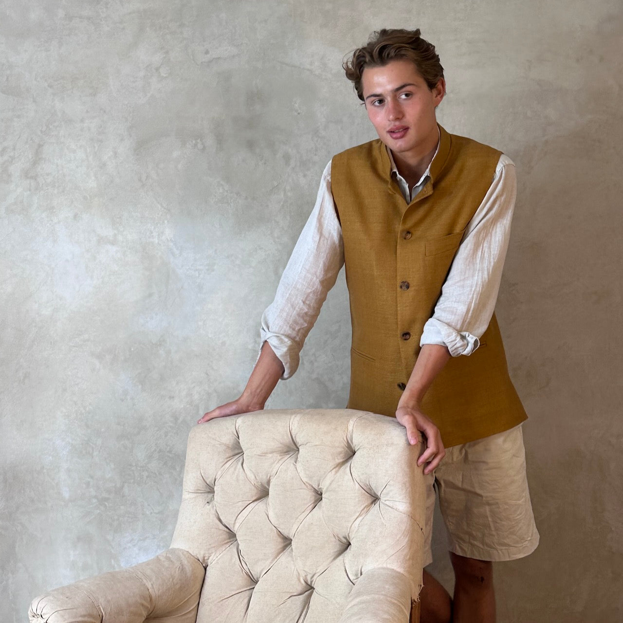 Tan coloured slim fit gilet in a summer weight silk weave. Handmade in London this fitted waistcoat has five pockets and a Nehru collar. Made in Great Britain. Modelled over cream co-ordinates.