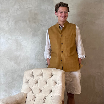 Tan coloured slim fit gilet in a summer weight silk weave. Handmade in London this fitted waistcoat has five pockets and a Nehru collar. Made in Great Britain. Modelled over cream co-ordinates.  The perfect alternative to a jacket on hotter days.