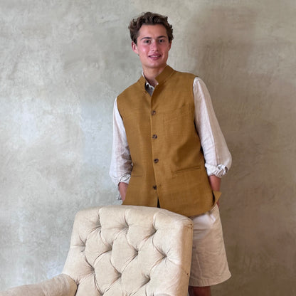 The perfect alternative to a jacket on hotter days. Tan coloured slim fit gilet in a summer weight silk weave. Handmade in London this fitted waistcoat has five pockets and a Nehru collar. Made in Great Britain. Modelled over cream co-ordinates.  