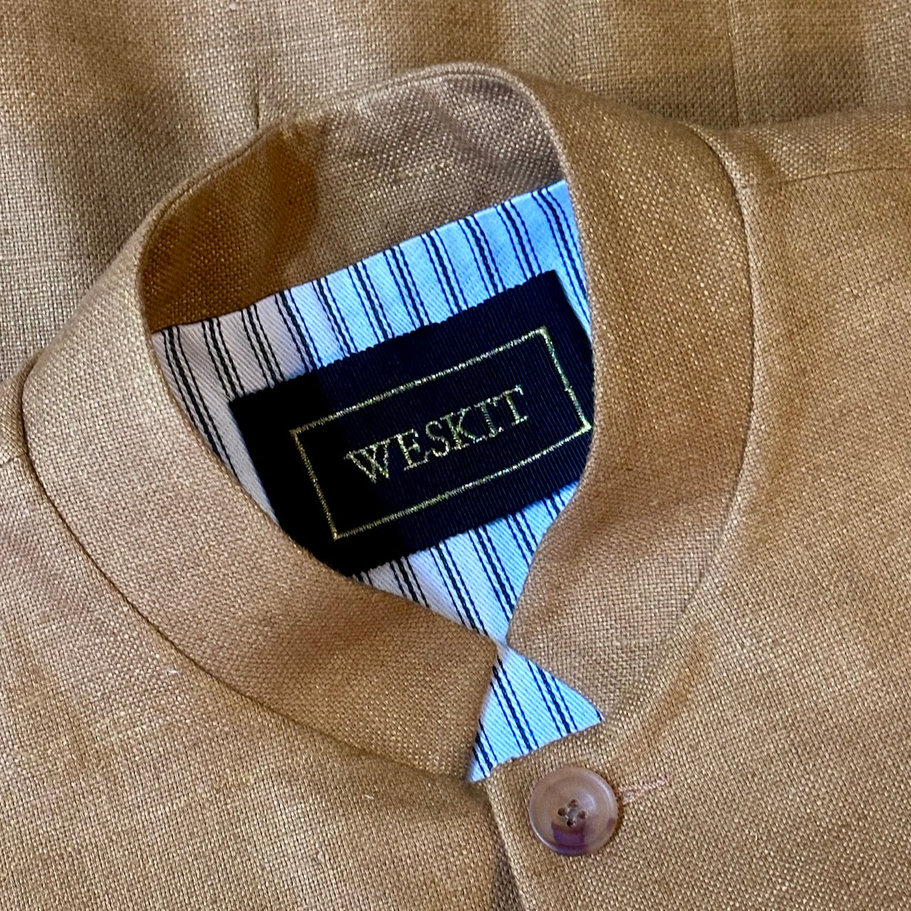 The perfect alternative to a jacket on hotter days, this summer weight slim fit gilet is handmade in London. Made up in a pure silk matka, the waistcoat is fitted and fully lined with two inside and three outside pockets. Close up shot showing gNehru collar, silk embroidered label and striped cotton ticking lining.
