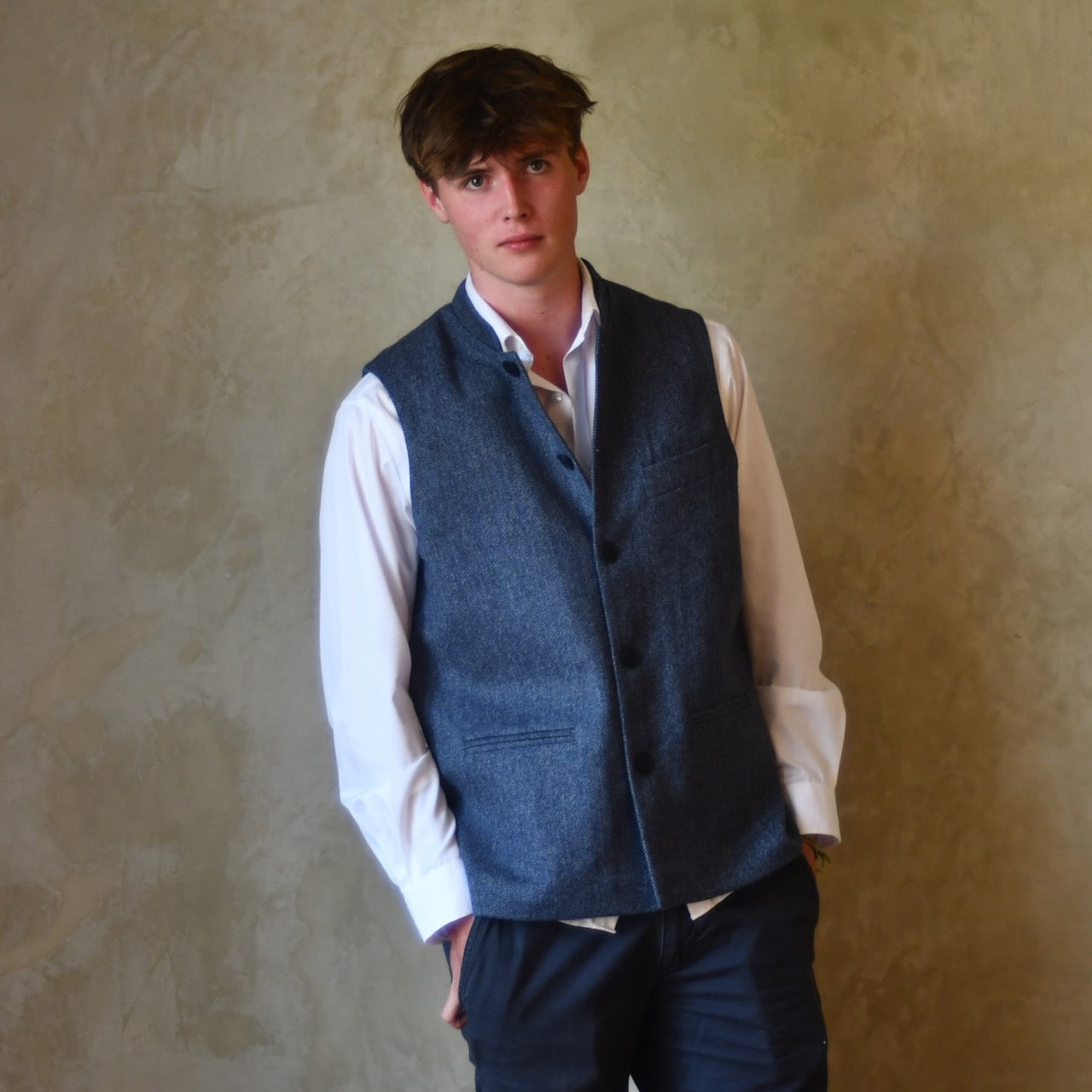 Loose Fit Nehru Style Gile in Demin Blue Herringbone Tweed. Handmade in London to order. Bespoke Sizing available. Shown buttoned over white shirt and blue trousers.