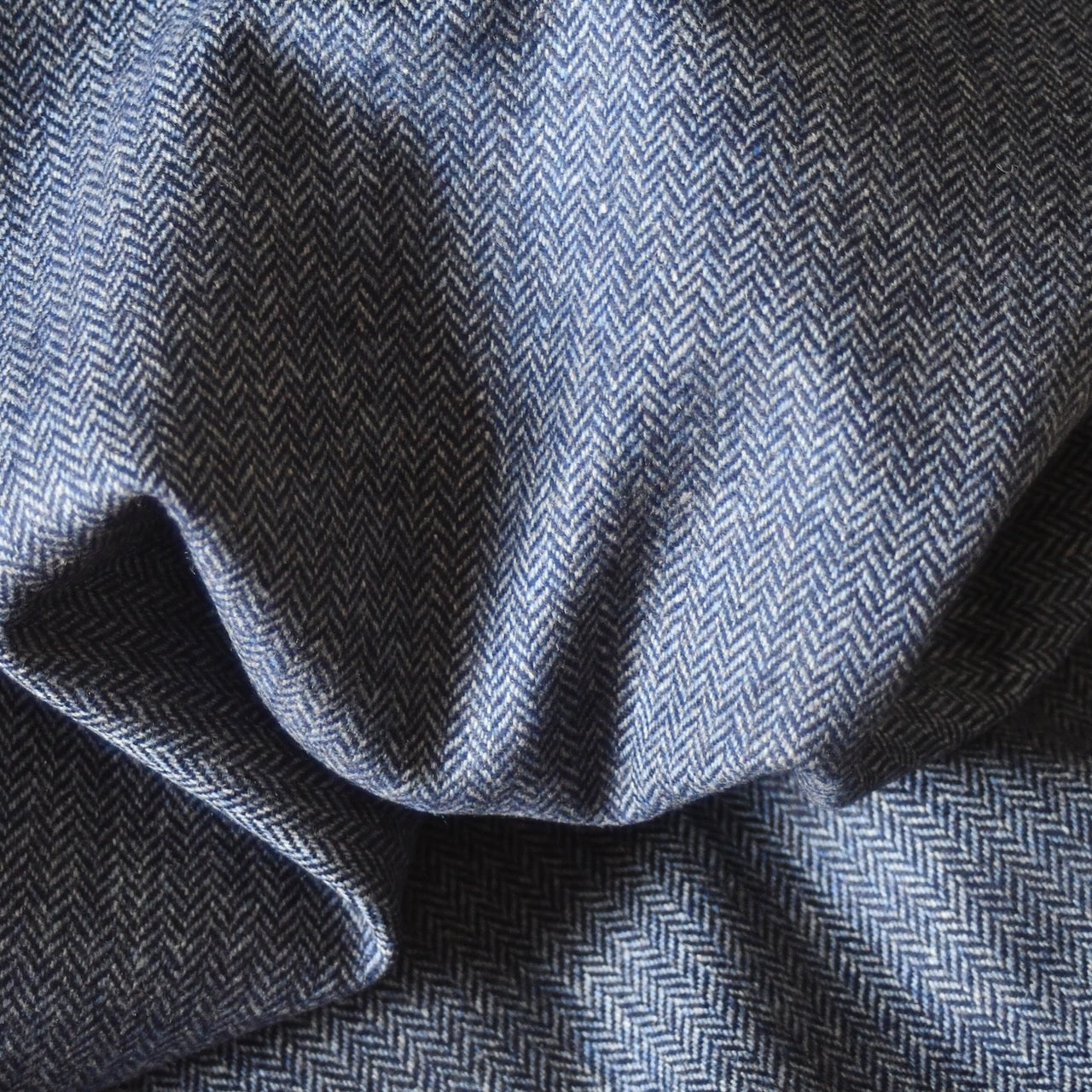 Fabric close up showing pure wool herringbone tweed in denim blue.