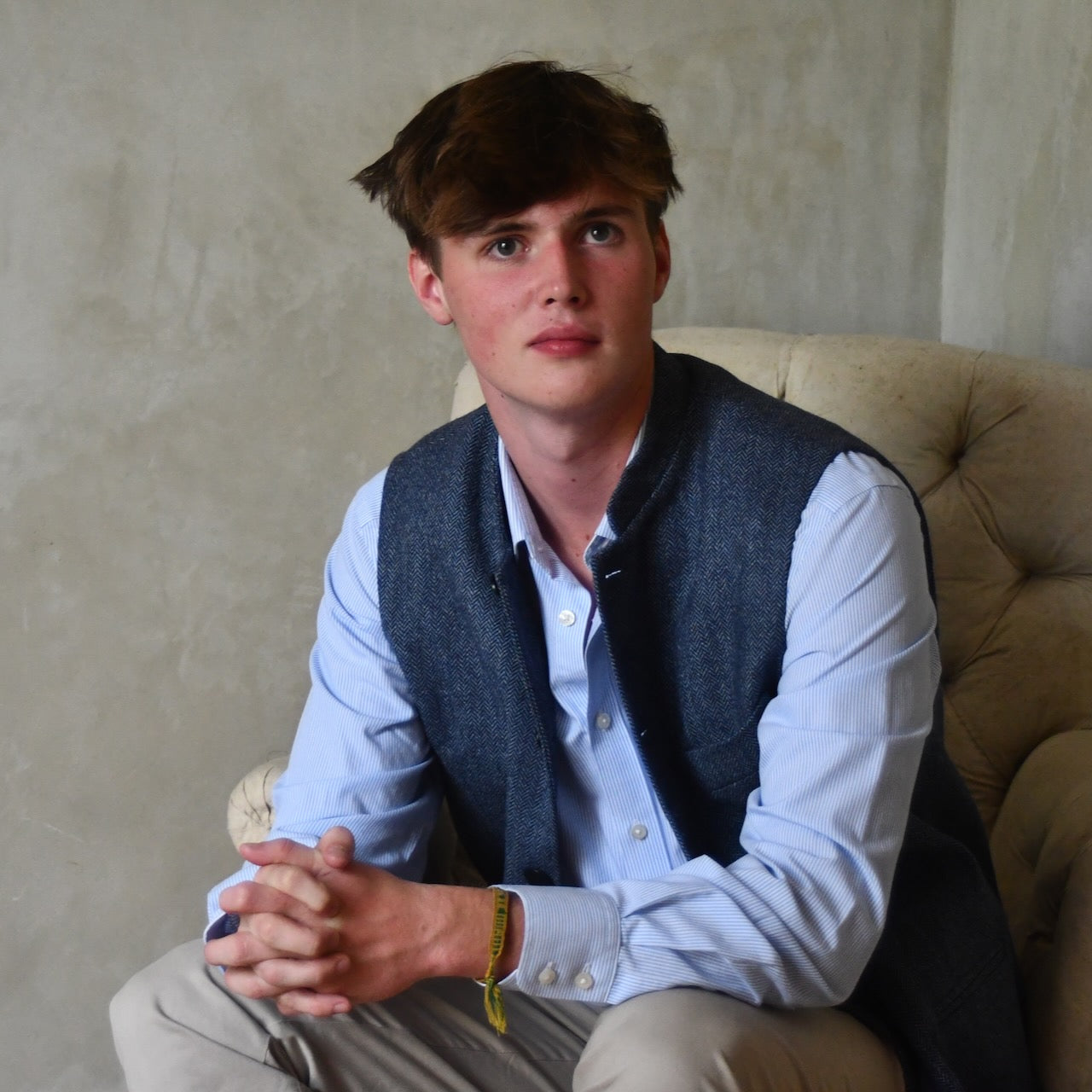 Loose Fit Nehru Style Gile in Demin Blue Herringbone Tweed. Handmade in London to order. Bespoke Sizing available. Shown seated and unbuttoned over blue shirt and blue trousers.