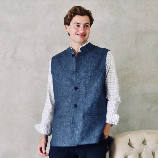 Fitted Cut Nehru-Style Gilet in Denim Blue Herringbone Tweed. A Tailored Cut waistcoat in magical mid-to-warmer weight lambswool tweed with a herringbone patterning.
Giving the overall effect of a delightful denim from a distance, this textiles brightens up on closer inspection as the depths and vivid colours of its patterning are revealed.
Smart, elegant and urbane – but as easy to match with jeans as it is to wear more formally.