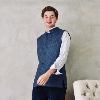 Fitted Cut Nehru-Style Gilet in Denim Blue Herringbone Tweed. A Tailored Cut waistcoat in magical mid-to-warmer weight lambswool tweed with a herringbone patterning.
Giving the overall effect of a delightful denim from a distance, this textiles brightens up on closer inspection as the depths and vivid colours of its patterning are revealed.
Smart, elegant and urbane – but as easy to match with jeans as it is to wear more formally.