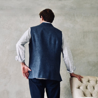 Fitted Cut Nehru-Style Gilet in Denim Blue Herringbone Tweed. A Tailored Cut waistcoat in magical mid-to-warmer weight lambswool tweed with a herringbone patterning.
Giving the overall effect of a delightful denim from a distance, this textiles brightens up on closer inspection as the depths and vivid colours of its patterning are revealed.
Smart, elegant and urbane – but as easy to match with jeans as it is to wear more formally. Rear View.