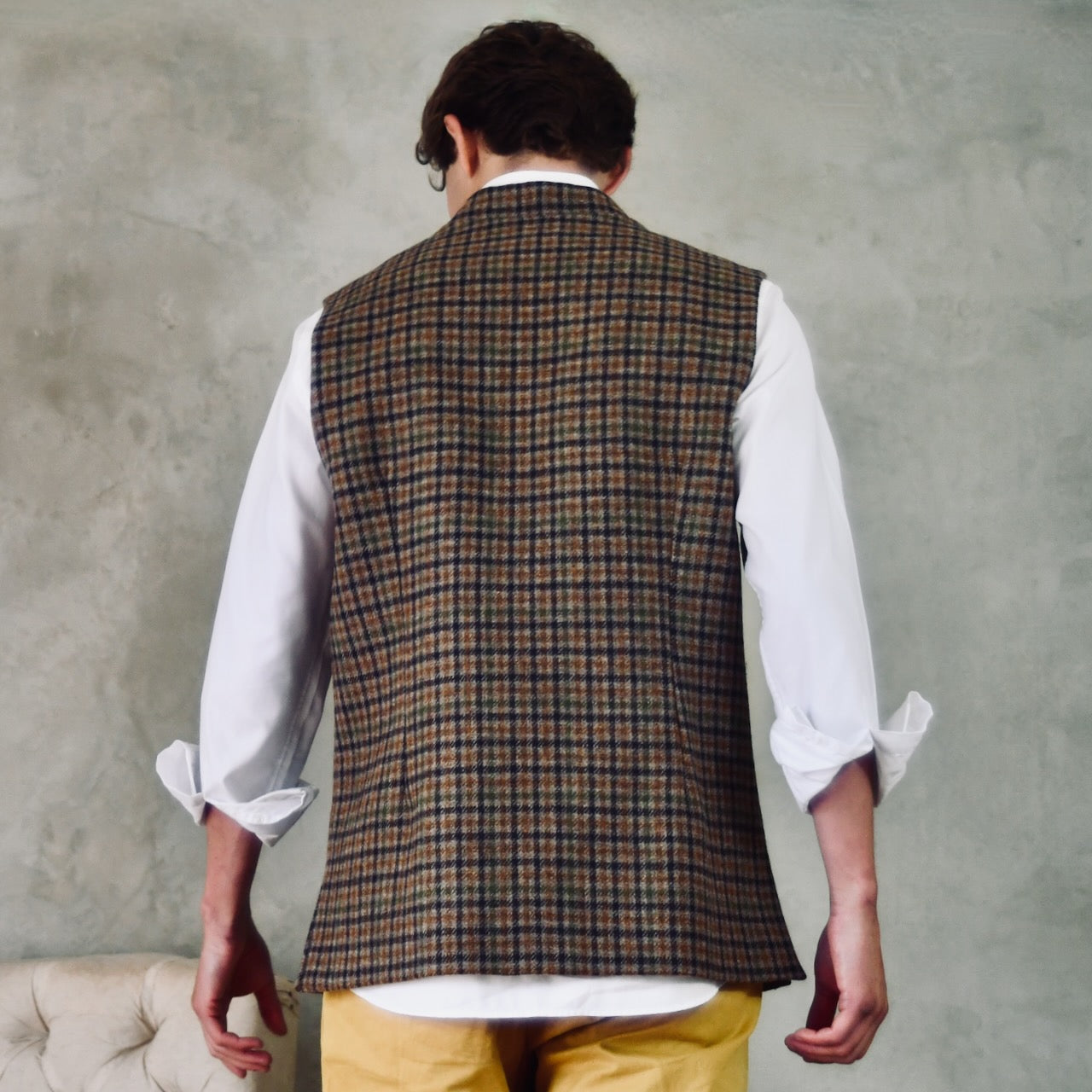 A superbly fine tweed that Nehru Style Gilet. Worth every penny, it will take you everywhere, smartly. A smokey brown and dull green weave a stunning check against a warm hued background, creating an unusual and bold check that will hold its own anywhere. Woven in Somerset, Cu. Made and Finished in London, this Gilet is entirely made in Great Britain. Full Back Shot showing darts and side vents.