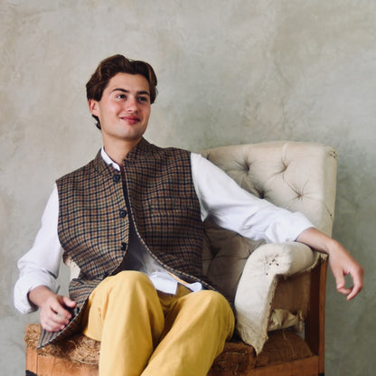 A superbly fine tweed that Nehru Style Gilet. Worth every penny, it will take you everywhere, smartly. A smokey brown and dull green weave a stunning check against a warm hued background, creating an unusual and bold check that will hold its own anywhere. Woven in Somerset, Cu. Made and Finished in London, this Gilet is entirely made in Great Britain. Seated Shot.