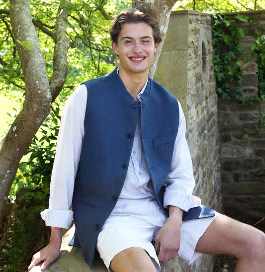 Nehru Style Gilet in Heavy Blue Linen. Irish Linen Gilet, Made by Hand in London. Entirely made in Great Britain. Seated Outside View.