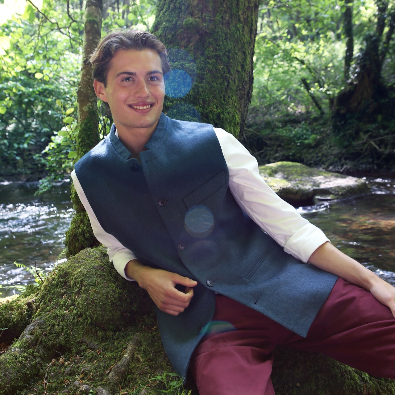Relaxed Fit Nehru Style Gilet in Heavy Blue Linen. Irish Linen Gilet, Made by Hand in London. Entirely made in Great Britain. Seated Shot by a river in Wales,