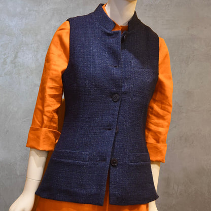 Ladies Shaped Gilet in Linton Tweeds boucle. A deep navy spring-summer weight fabric, this gilet packs superbly and can be worn everywhere. Handmade in London. Open Shot shown over orange lightweight linen dress from EdNerat.