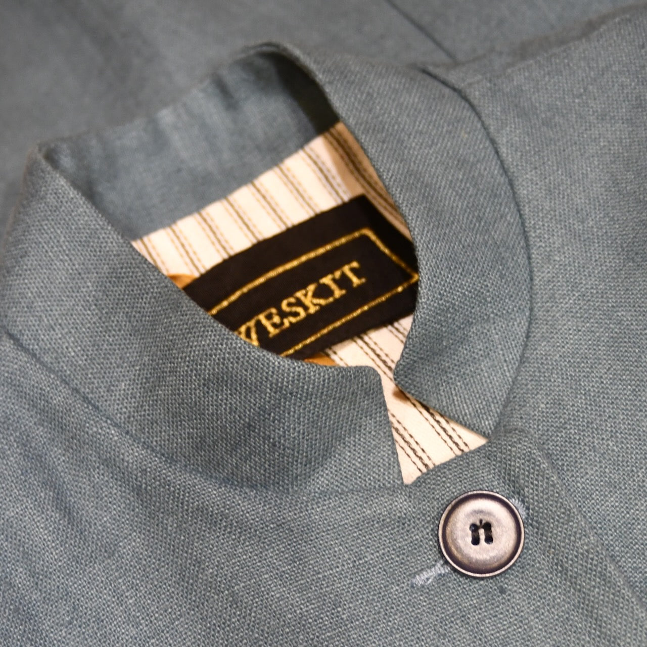 Collar detail showing Weskit Embroidered silk label on Ladies Gilet in Light Blue Irish Linen. Handmade in London this waistcoat has a Nehru collar, cotton ticking lining, bust darts as well as front and rear waist-shaping darts. Shown over mustard coloured EdNerat dress.