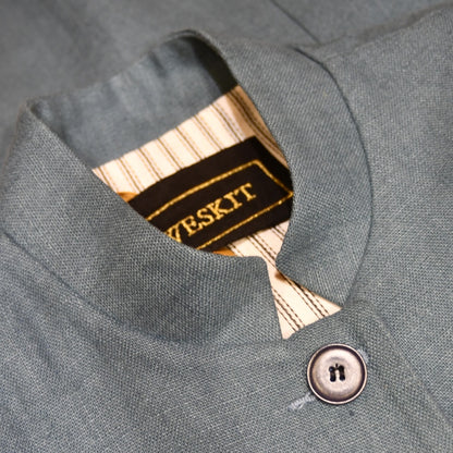 Collar detail showing Weskit Embroidered silk label on Ladies Gilet in Light Blue Irish Linen. Handmade in London this waistcoat has a Nehru collar, cotton ticking lining, bust darts as well as front and rear waist-shaping darts. Shown over mustard coloured EdNerat dress.