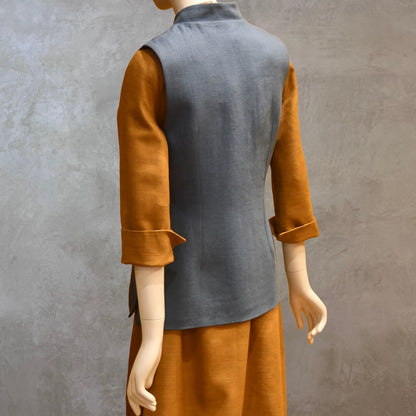 Rear Angled Shot of Ladies Gilet in Light Blue Irish Linen. Handmade in London this waistcoat has a Nehru collar, cotton ticking lining, bust darts as well as front and rear waist-shaping darts. Shown over mustard coloured EdNerat dress.