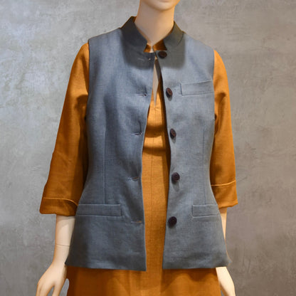 Unbuttoned shot of Ladies Gilet in Light Blue Irish Linen. Handmade in London this waistcoat has a Nehru collar, cotton ticking lining, bust darts as well as front and rear waist-shaping darts. Shown over mustard coloured EdNerat dress.