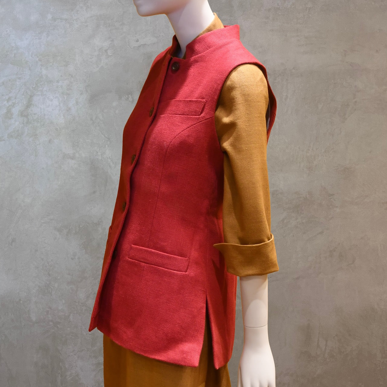 Side Buttoned up shot of Ladies Shaped Gilet in Red Irish linen. Handmade in London the waistcoat is shown worn over a mustard coloured silk dress by EdNerat.