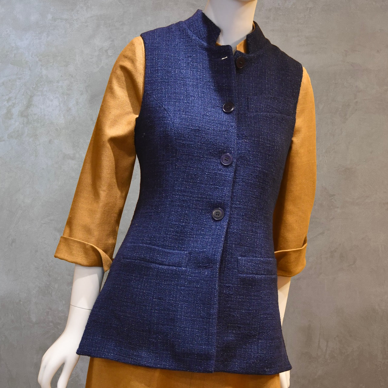 Longer Length Ladies Gilet in Linton Tweeds Boucle. A pure cotton weave,  this is superbly trans-seasonal option. Handmade in London. Front on Shot shown over mustard coloured Silk Matka Dress from Ednerat.