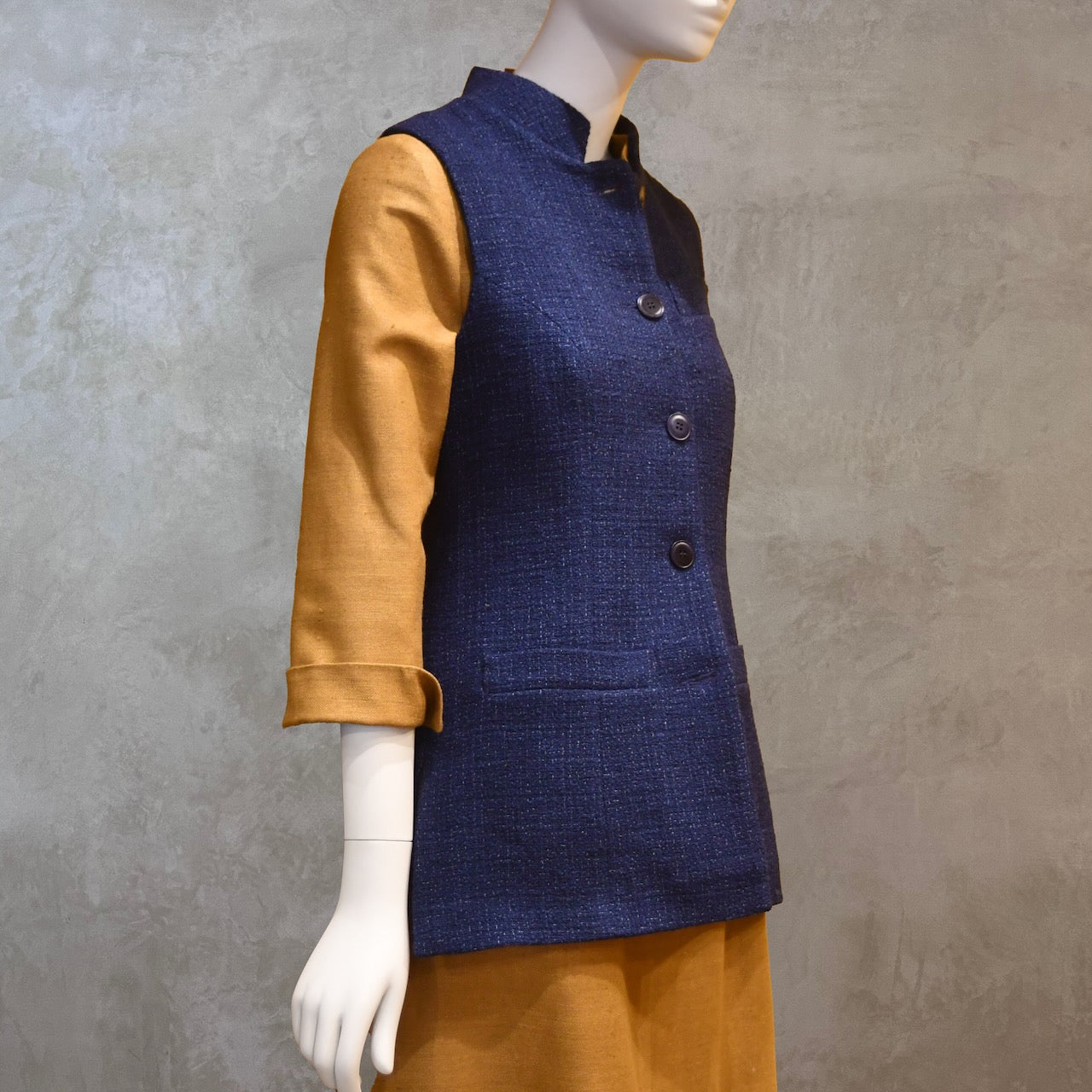 Longer Length Ladies Waistcoat in Linton Tweeds Boucle. A pure cotton weave,  this is superbly trans-seasonal option. Handmade in London. Side Shot shown over mustard coloured Silk Matka Dress from Ednerat.