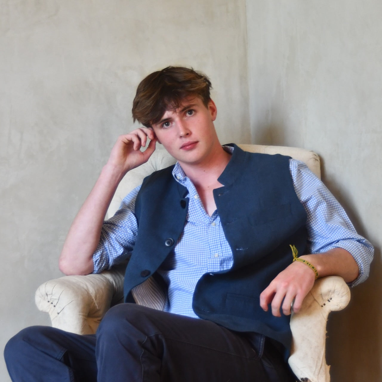 Seated view of Navy Linen Fitted Cut Waistcoat. A bespoke Pure Irish Linen waistcoat, handmade in London. Lined in pure cotton ticking with a Nehru collar. Worn over a blue shirt, 