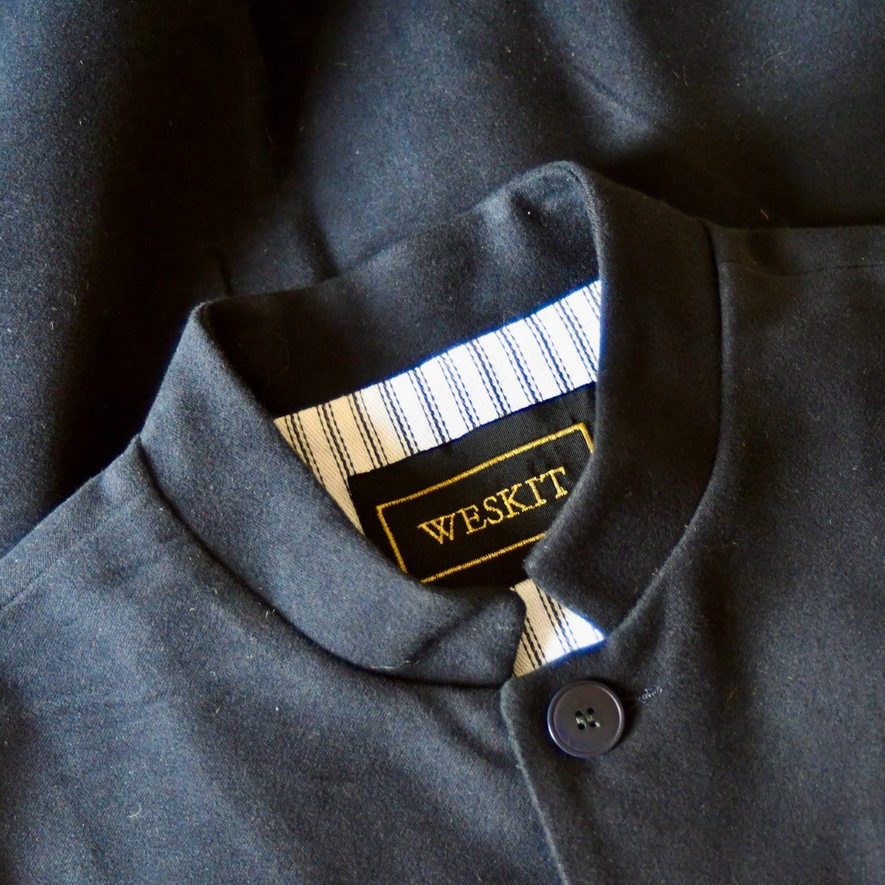 Detail collar view of Nehru style gilet in navy moleskin. A bespoke slim-fit gilet in a pure cotton navy moleskin fabric handmade for you in London. Detail shot shows Nehru Collar, Cotton Ticking Lining and Black silk embroidered label.