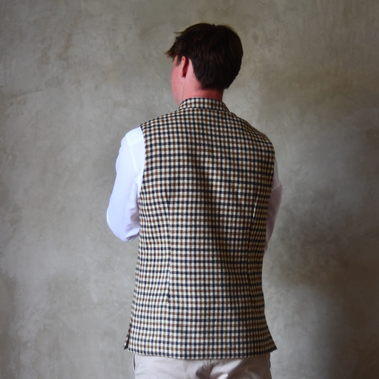 Rear view of Fitted Nehru-style gilet in pure wool tweed. This gunclub check tweed waistcoat has a softer than usual feel, being made from fabric woven in Somerset. Handmade in London these waistcoats can be ordered in size 26 to 54 and bespoke sizes.