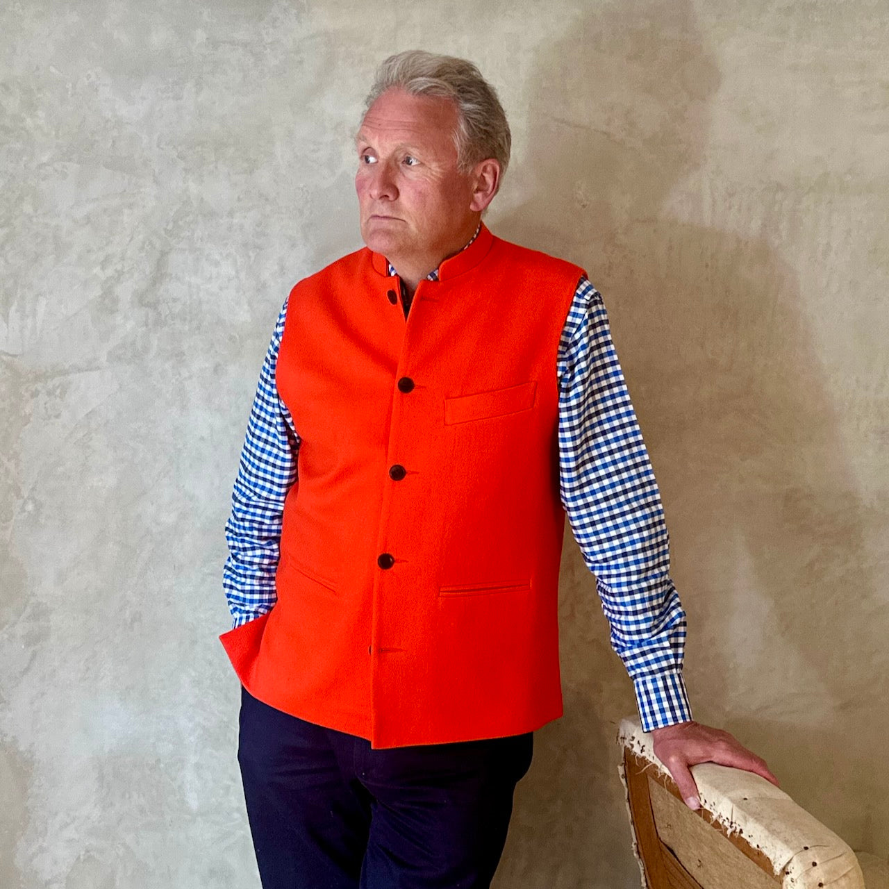 A bright orange Nehru Style Gilet in pure merino wool flannel. Woven in Yorkshire this merino melton has a wonderful handle and a lovely warm weight to it. Handmade in London, this gilet has three outer and two inner pockets and side vents for ease when seated.
Cut,  Made and Finished by Hand in London. Woven in Yorkshire, with buttons from Gloucestershire - a truly British Waistcoat. Worn over blue and white checked shirt.