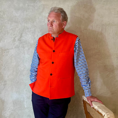 A bright orange Nehru Style Gilet in pure merino wool flannel. Woven in Yorkshire this merino melton has a wonderful handle and a lovely warm weight to it. Handmade in London, this gilet has three outer and two inner pockets and side vents for ease when seated.
Cut,  Made and Finished by Hand in London. Woven in Yorkshire, with buttons from Gloucestershire - a truly British Waistcoat. Worn over blue and white checked shirt.