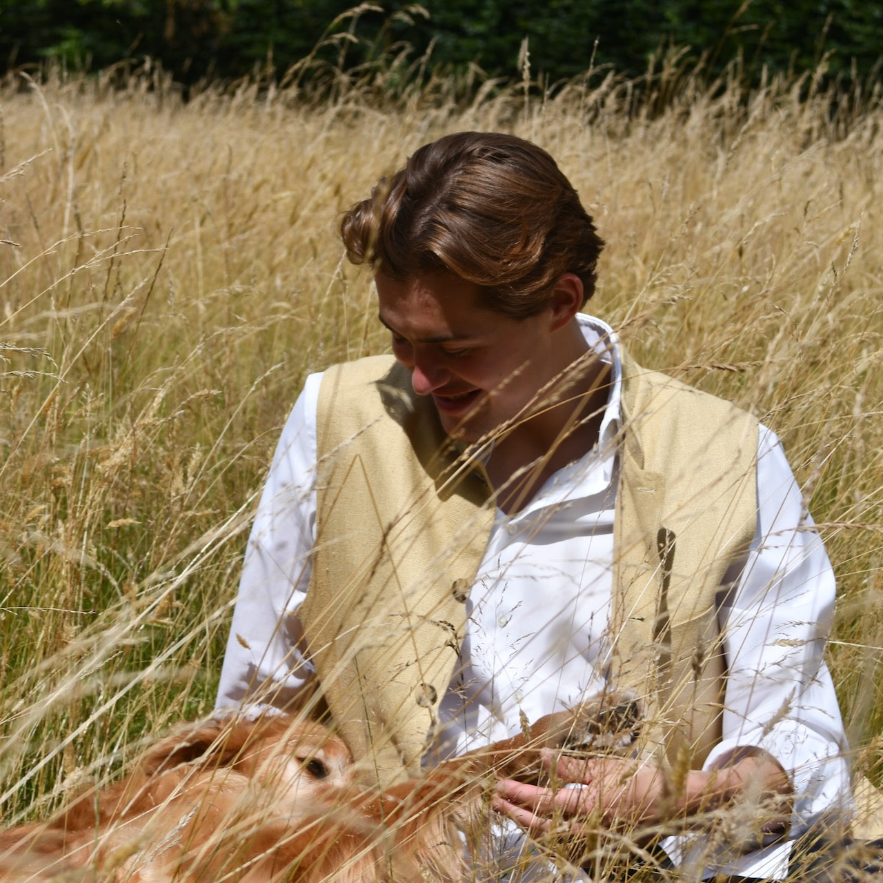 Lighter weight fitted gilet in sandy straw coloured silk weave fabric. Handmade in London this Nehru style gilet boast a Nehru collar, five pockets and is fully lined in pure cotton ticking. Seated unbuttoned shot.