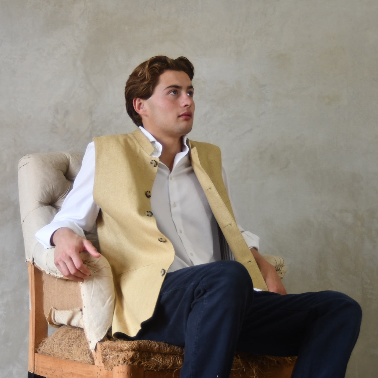 Lighter weight fitted gilet in sandy straw coloured silk weave fabric. Handmade in London this Nehru style gilet boast a Nehru collar, five pockets and is fully lined in pure cotton ticking. Seated Unbuttoned Shot.