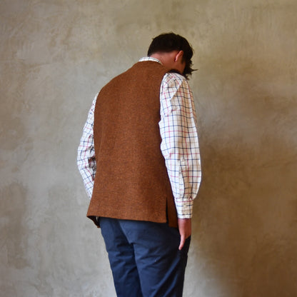 Rear view of Bespoke Waistcoat in pure wool tweed in russet brown. Handmade in London, this Nehru-style gilet is shown worn over a checked shirt and blue chino trousers.