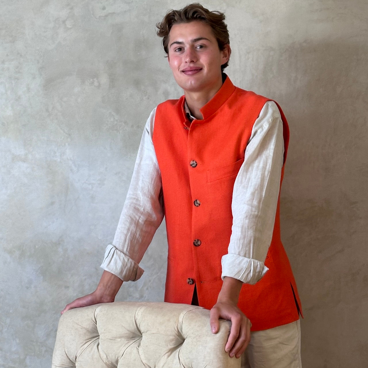 Slim fit nehru style gilet in summer weight silk weave fabric. Handmade in London, this orange silk matka fitted waistcoat has a Nehru collar, Courtney & Co buttons and is fully lined in striped cotton ticking. Standing Buttoned Shot.