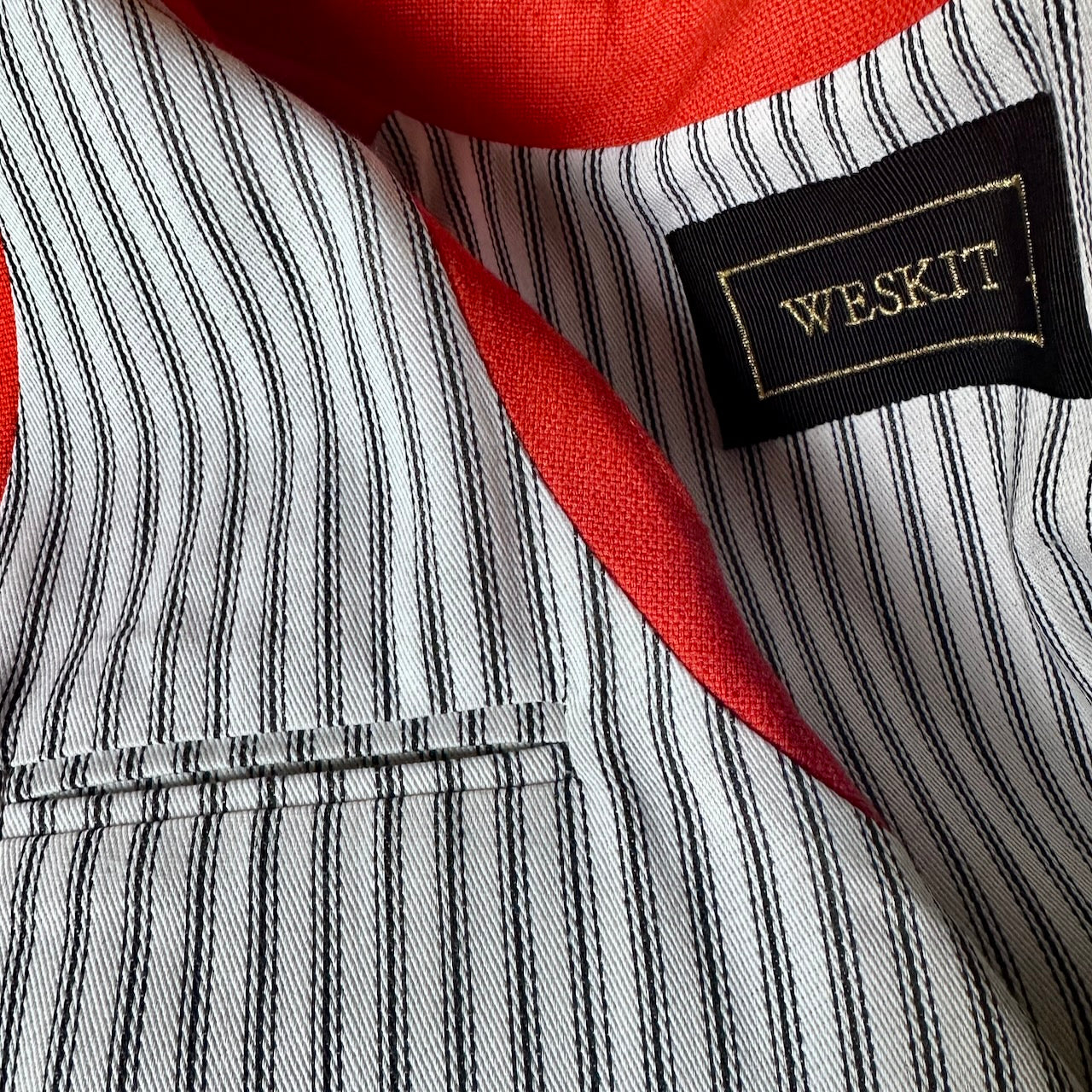 Close up on lining, label and inside pocket of Slim fit nehru style gilet in summer weight silk weave fabric. Handmade in London, this orange silk matka fitted waistcoat has a Nehru collar, Courtney & Co buttons and is fully lined in striped cotton ticking. 