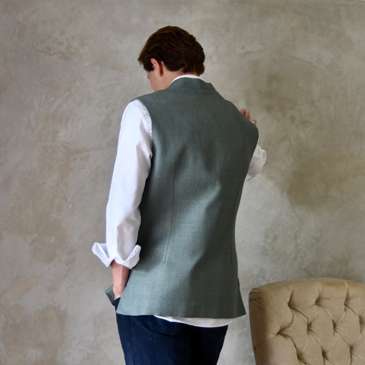 Rear view of Slim cut summer weight nehru style gilet in pale green silk weave. Handmade in London this fitted waistcoat has a Nehru  collar and is fully lined in cotton ticking. Real horn buttons. Rear Shot.