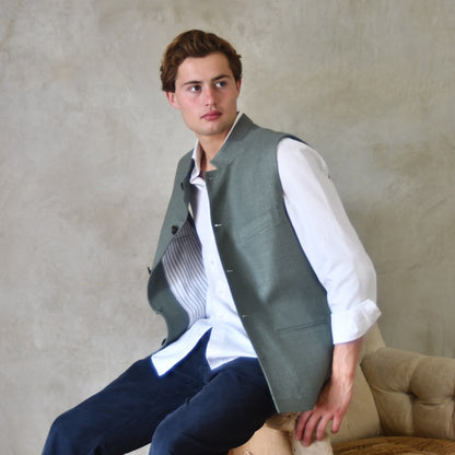 Slim cut summer weight nehru style gilet in pale green silk weave. Handmade in London this fitted waistcoat has a Nehru  collar and is fully lined in cotton ticking. Real horn buttons. Seated View.