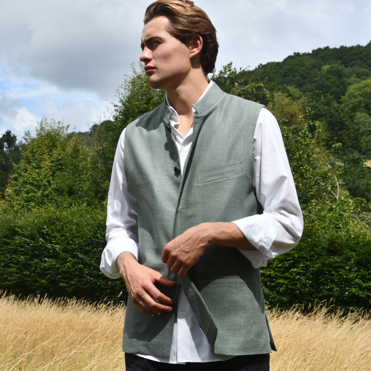 Slim cut summer weight nehru style gilet in pale green silk weave. Handmade in London this fitted waistcoat has a Nehru  collar and is fully lined in cotton ticking. Real horn buttons. Shot outside in summer.