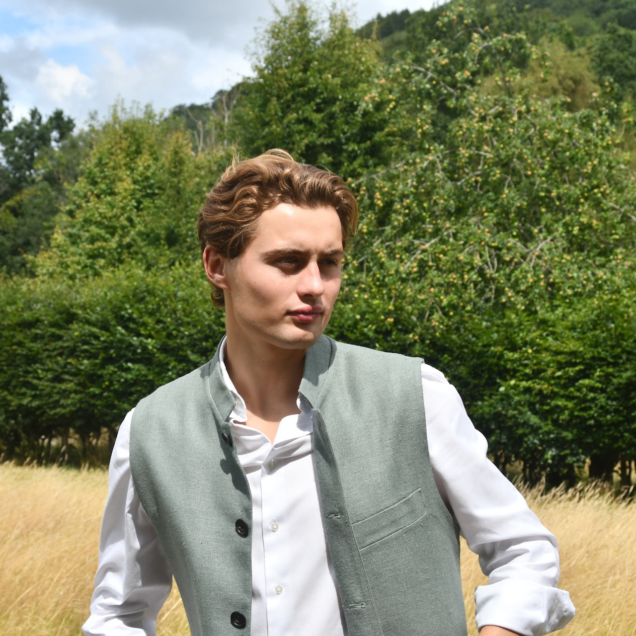 Slim cut summer weight nehru style gilet in pale green silk weave. Handmade in London this fitted waistcoat has a Nehru  collar and is fully lined in cotton ticking. Real horn buttons. Shot outside in summer.